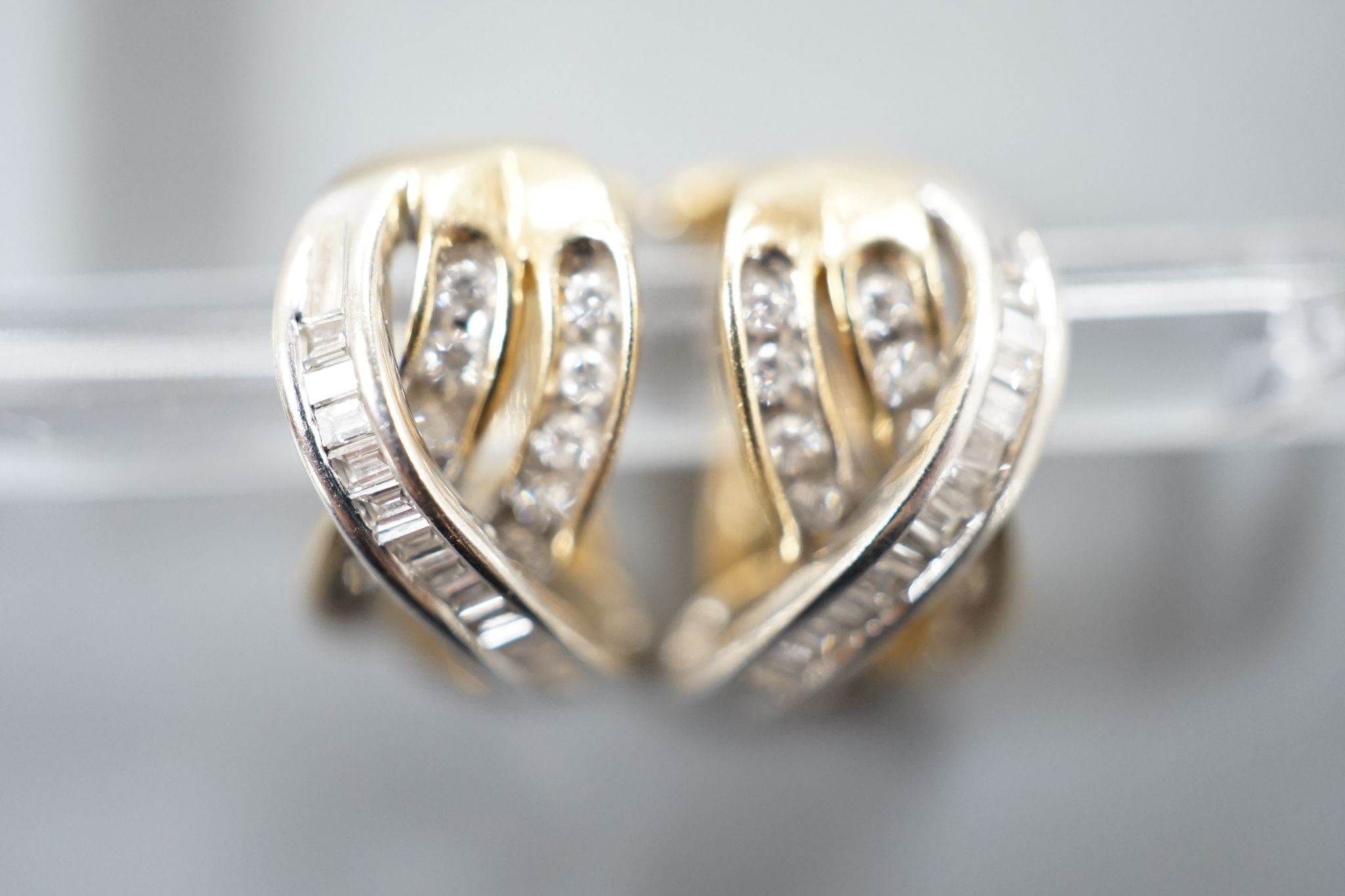 A modern pair of 14k, round and baguette cut diamond set triple row crossover earrings